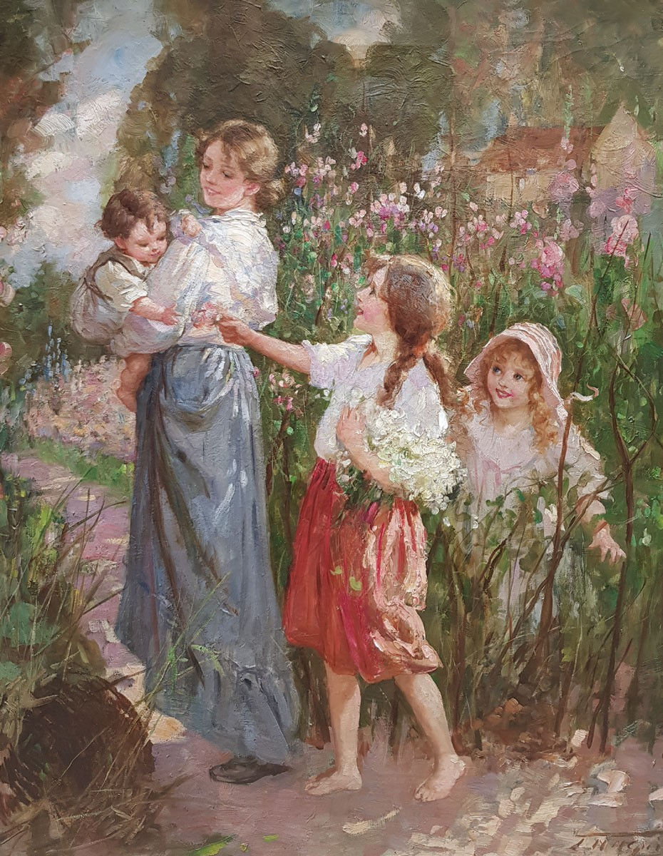 A woman in a white blouse and blue dress holds an infant in her arms with two young girls following behind her as they walk through along a path lined with tall pink flowers