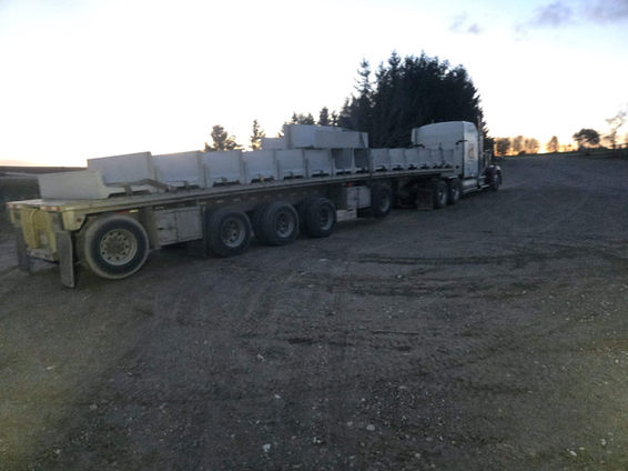 View-con precast concrete large J cattle feed bunks loaded on a flatbed trailer at dusk, staged for delivery from a rural yard.