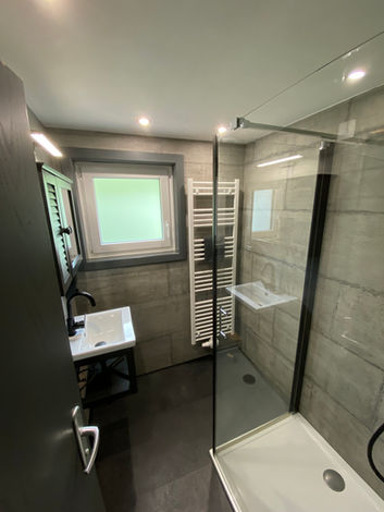 Modernes Badezimmer mit Glasdusche, Waschbecken, schlichten Fliesen und hellem Fenster.