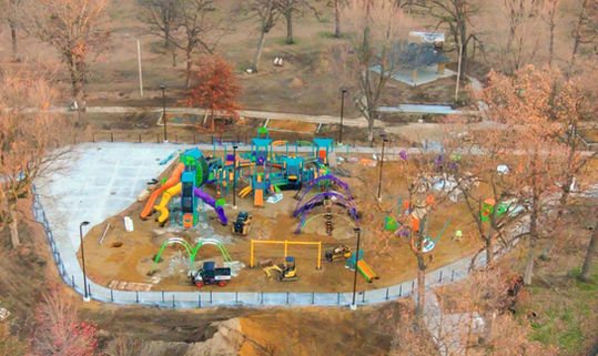 Aerial view of a vibrant playground, surrounded by trees and pathways, outside.