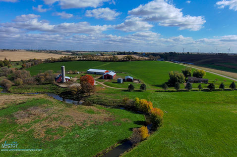 Aerial view of a farm, with red barn, green fields, and blue skies.