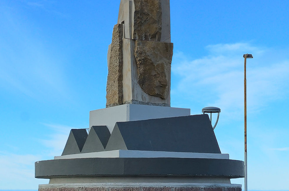 fotografia de una escultura de piedra en una rotonda de san julian, en el fondo se ve la bahia y el cielo celeste con pocas nuves.