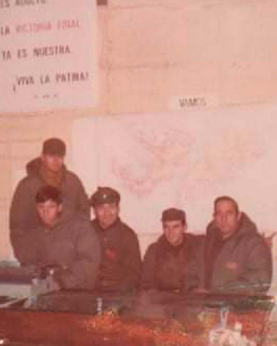 Esta fotografía es del interior de el argensud, donde se ve posando a 5 militares sentados en un escritorio, detrás se pueden ver mapas colgados en un muro.