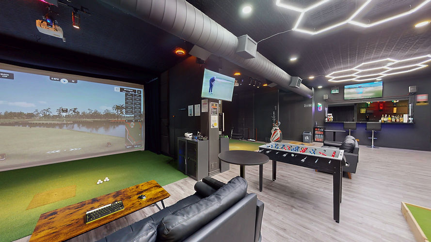 Wide view of the lobby. Front of bay 2, foosball table, bar, and wall mounted tv displaying a golf program is shown.