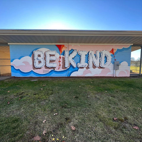 Be Kind Mural with blue sky, clouds, and kites