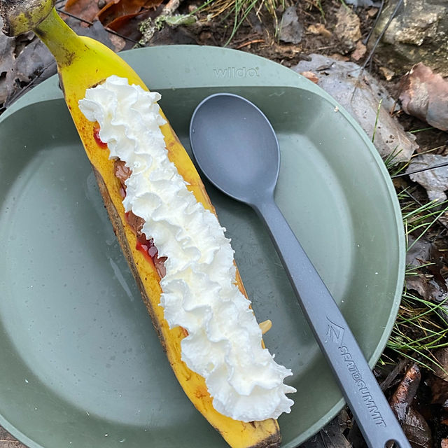 grønn turtallerken og plastskje med banan stekt på primus med pisket krem topping