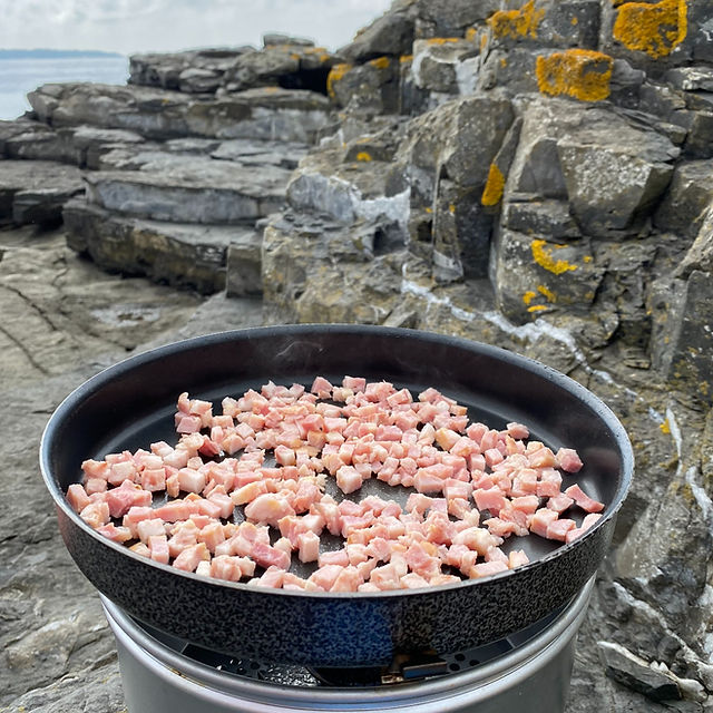 Trangia stormkjøkken i fjære med baconbiter som steker i en stekepanne