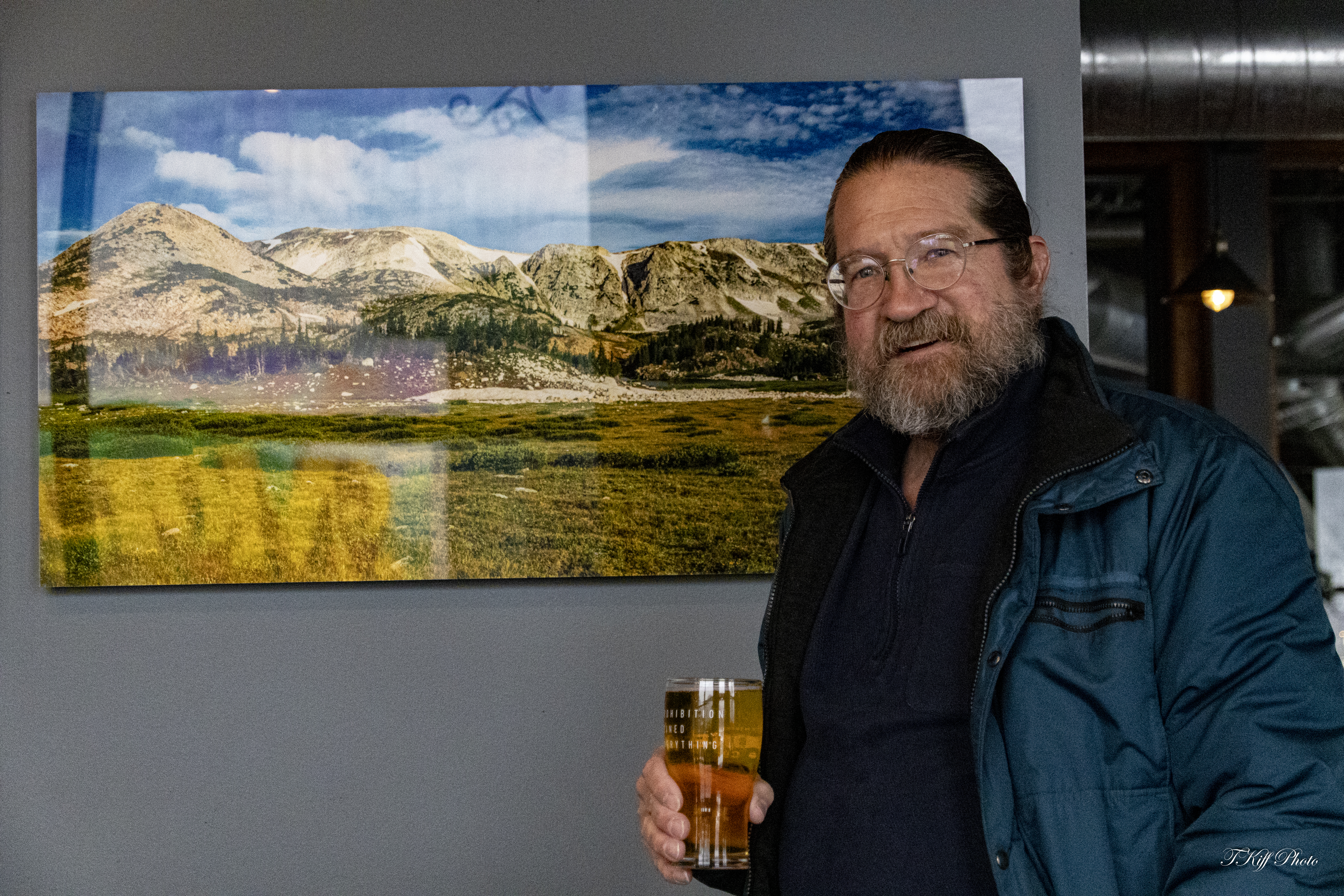 A man stands in front of a nature print with a drink.  