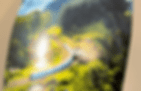 On metallic paper, a blue train winding through lush green hills under a bright sky, surrounded by dense tall trees; sunlight creates a serene atmosphere.