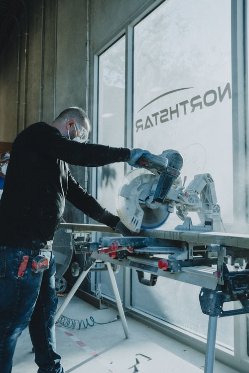 A carpenter cutting wood with saw, Northstar Building Systems visible in background.