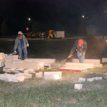 Construction workers sawing concrete blocks at night, creating dust, for a project.
