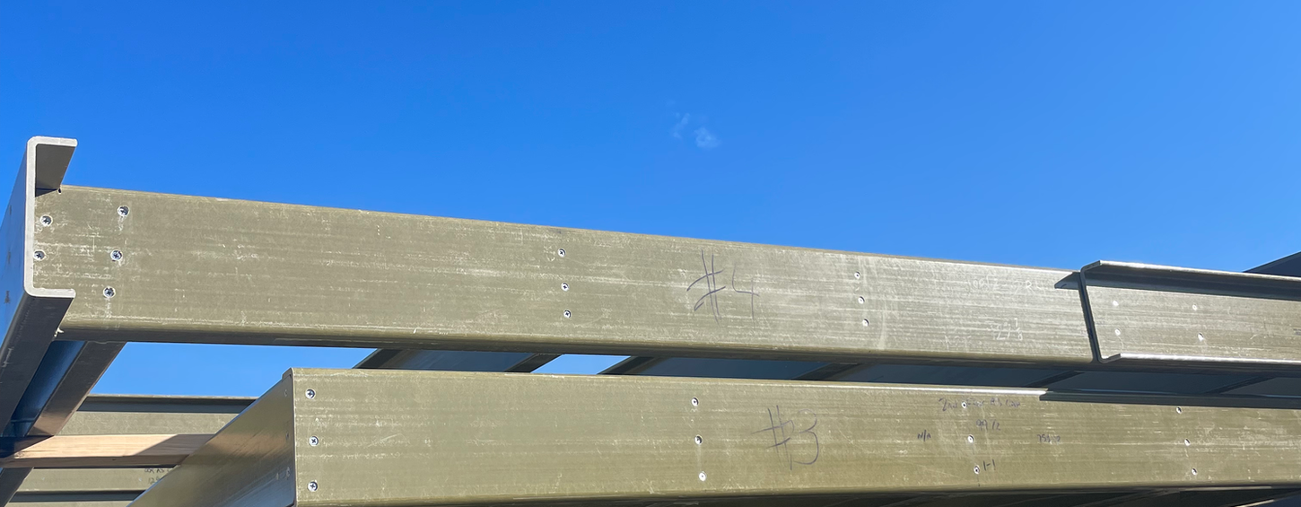 Steel beams stacked outdoors under a clear blue sky, ready for construction.