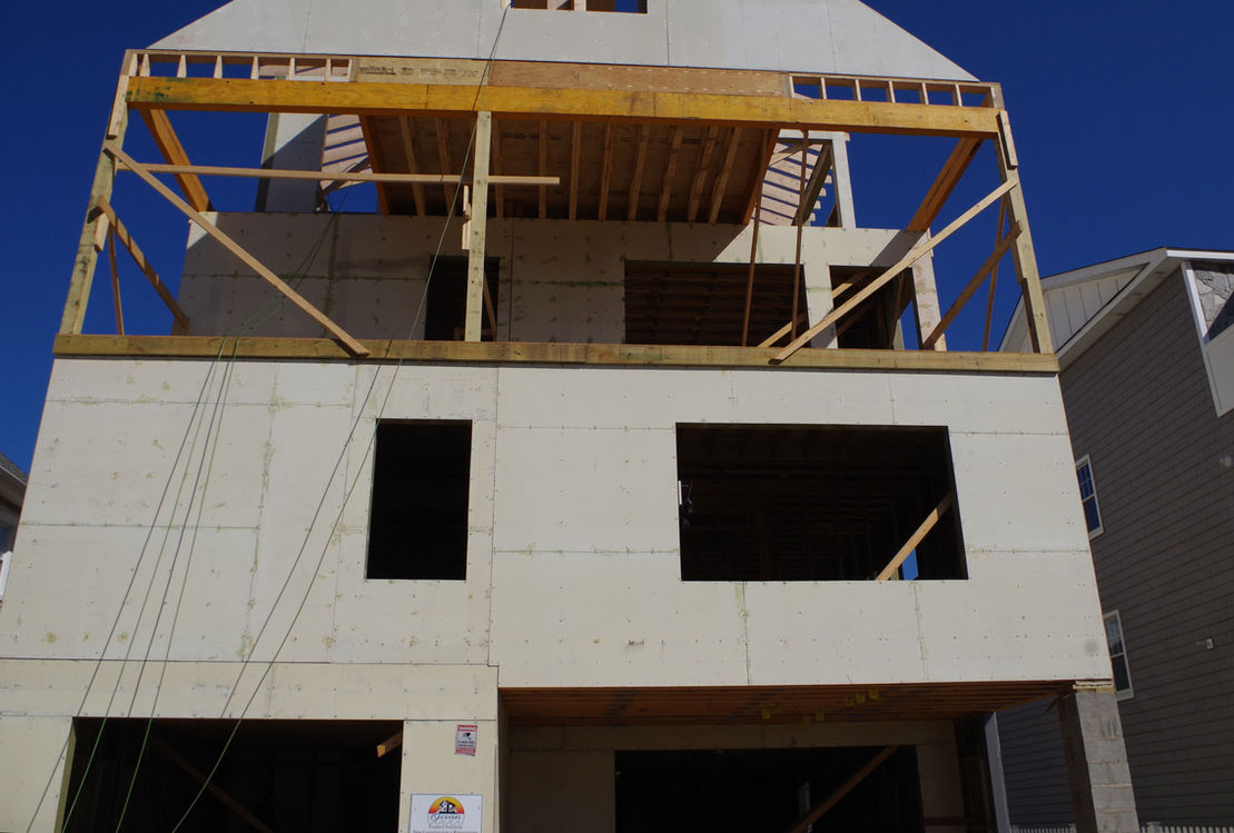 Wooden structure under construction with openings for windows, clear blue sky.