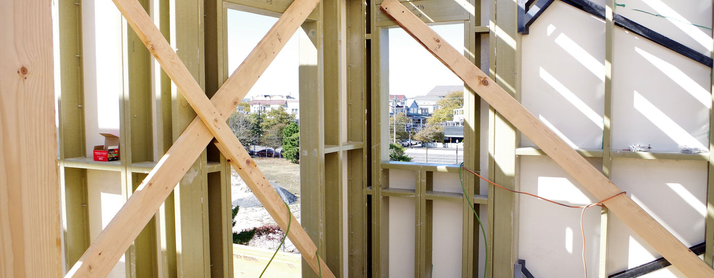 Wooden frame construction with bracing, window openings, and scenic background of trees.