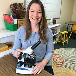 A smiling Montessori STEM teacher holds a microscope.