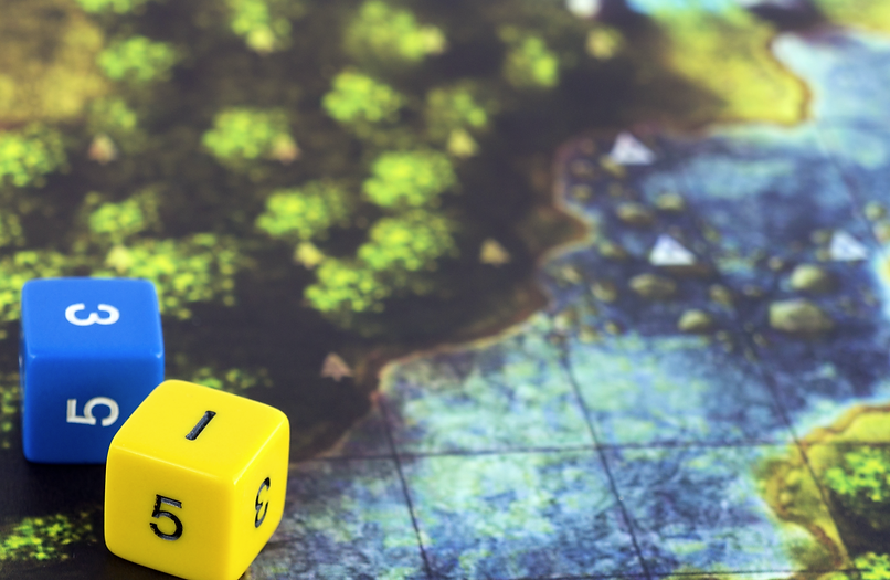 A Dungeons and Dragons board up close showing green bushes and blue sea with blue and yellow dice in the forefront of the image