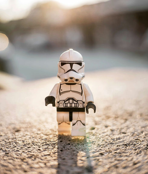 A stormtrooper lego figure walking forward toward the camera in a sandy scene.