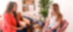 A female therapist with long curly brown hair and coral cardigan holding a remote control controlling EMDR tappers and next to an EMDR light bar with the tappers being held by a girl with long blode hair sat smiling in a chair.
