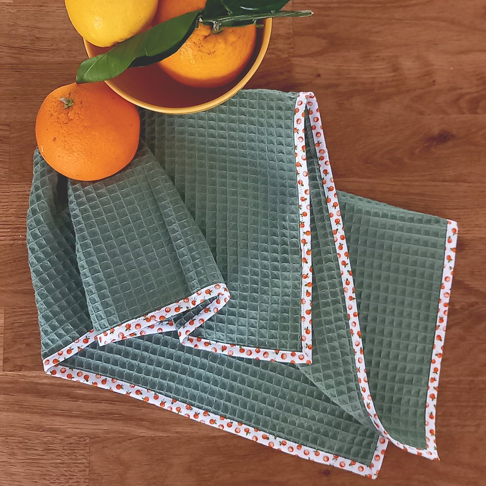 Torchon vert amande en coton nid d'abeille avec galon motifs oranges posé sur le plan de travail avec des agrumes