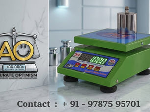A green digital weighing scale displays "100.00g" with weights on top. Logo: "AO Accurate Optimism." Contact: +91 - 97875 95701.