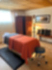 Picture of the massage studio the well heart with a massage table and stained glass lamp lighting the room with a glow.