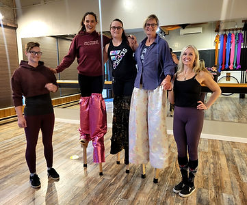 Three stiltwalkers in a classroom being supported on each side of the group