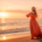 Woman in flowing dress playing violin on beach at sunset