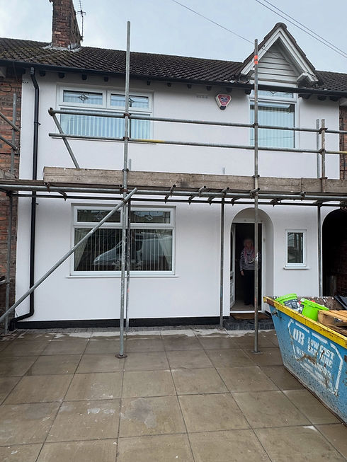 Two-storey white house exterior surrounded by metal scaffolding with a skip on the driveway