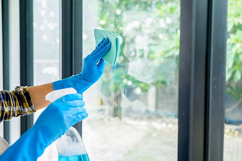 Gloved hands clean a window with a spray bottle and sponge
