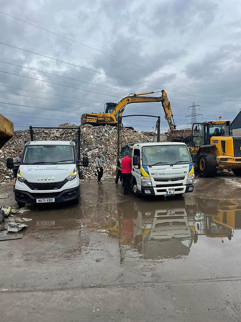 wo white waste management trucks parked in a recycling yard with heavy machinery