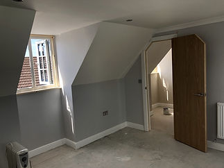 Newly plastered attic room with sharp angles, an open doorway, and a small window