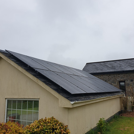 Solar panels on a sloped beige roof, adjacent to a stone building