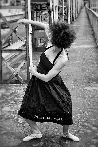 Woman with curly hair wearing a black halter-neck dress posing on a metal bridge