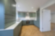 Modern U-shaped kitchen with dark blue cabinetry white countertops and light oak parquet flooring