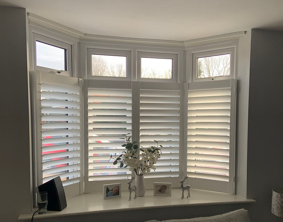 White plantation shutters covering the lower section of a multi-panel bay window with decorative items