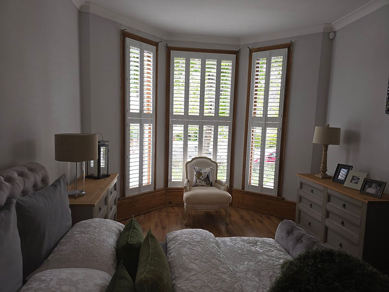 Living room bay window with white plantation shutters and a comfortable armchair in the centre