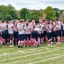 A large football team in uniform huddling together on a grassy field.