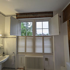 Bathroom with white tiled walls and window featuring half-height shutters and an exposed beam