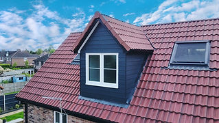 A house roof with red tiles features a small dormer with white-framed windows