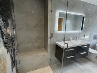 Walk-in shower area with a rain shower head built-in seat and a glass screen separating it from the vanity area