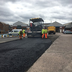 Road workers in new tarmac® in a commercial area car park using an asphalt paving machine