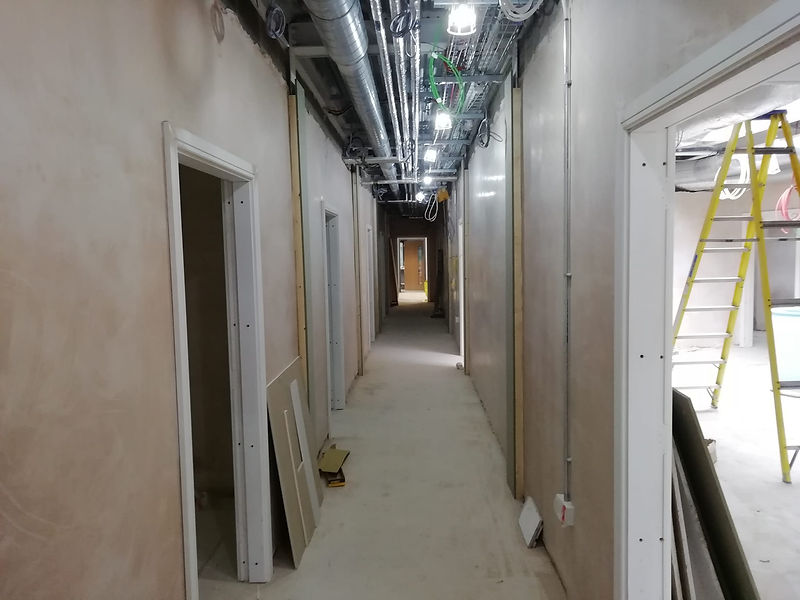Long corridor in a building under construction with exposed pipes, wiring, and freshly skimmed walls