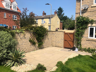 Light stone patio paving and timber gate in a sunny back garden