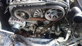 Close-up of a car engine showing the worn timing belt system with cogs and tensioners
