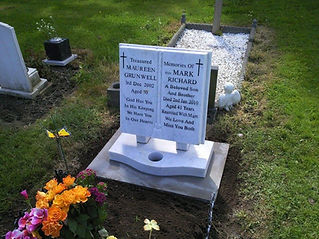 A double headstone in a graveyard with inscriptions for Maureen and Mark, surrounded by grass