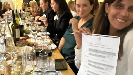 Smiling professional woman holding a tasting menu at a candlelit dinner party with wine glasses and guests