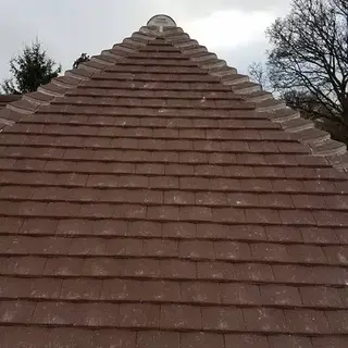 Close-up of a newly installed brown tiled hip roof meeting at a point against an overcast sky