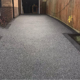 Freshly laid grey gravel driveway enclosed by brick walls and dark stone edgings