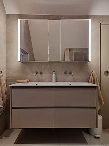 Taupe double basin vanity unit with wall-mounted taps and an illuminated mirrored cabinet above