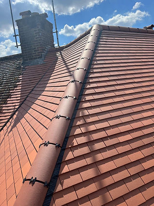 Terracotta clay roof tiles with a central ridge line and mechanical fixings